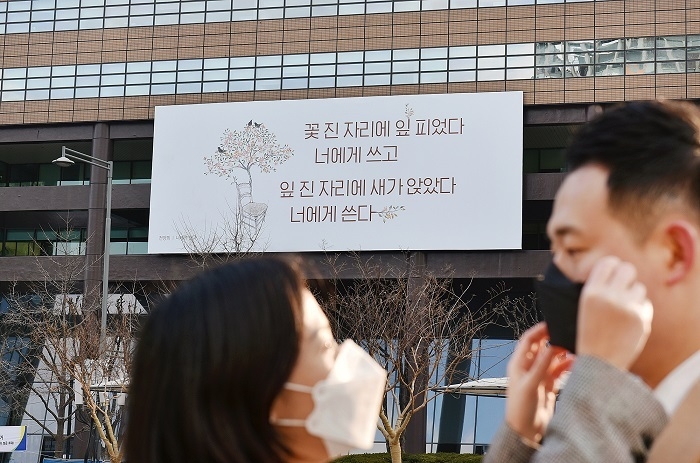  2일 교보생명 광화문글판 '봄편'이 내걸린 광화문 교보생명빌딩 주변에서 시민들이 마스크를 씌워주고 있다. 이번 문안은 천양희 시인의 시 ‘너에게 쓴다’에서 가져왔다. 아름다운 꽃이 진 곳에 새 생명이 다시 자라나는 자연의 순리를 보며 지난 것에 대한 아쉬움보다 내일의 희망을 기대하자는 메시지를 담았다. (사진=교보생명)