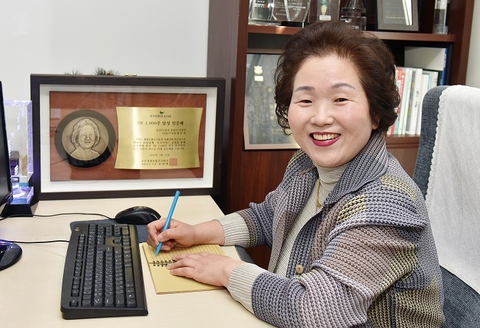 1000주 연속으로 매주 3건 계약을 맺은 정금옥 교보생명 FP프라임리더가 자신의 사무실에 앉아 환하게 웃고 있다. 그의 뒤로 '3W 1000주 달성 인증패'가 놓여있다. (사진=교보생명) 